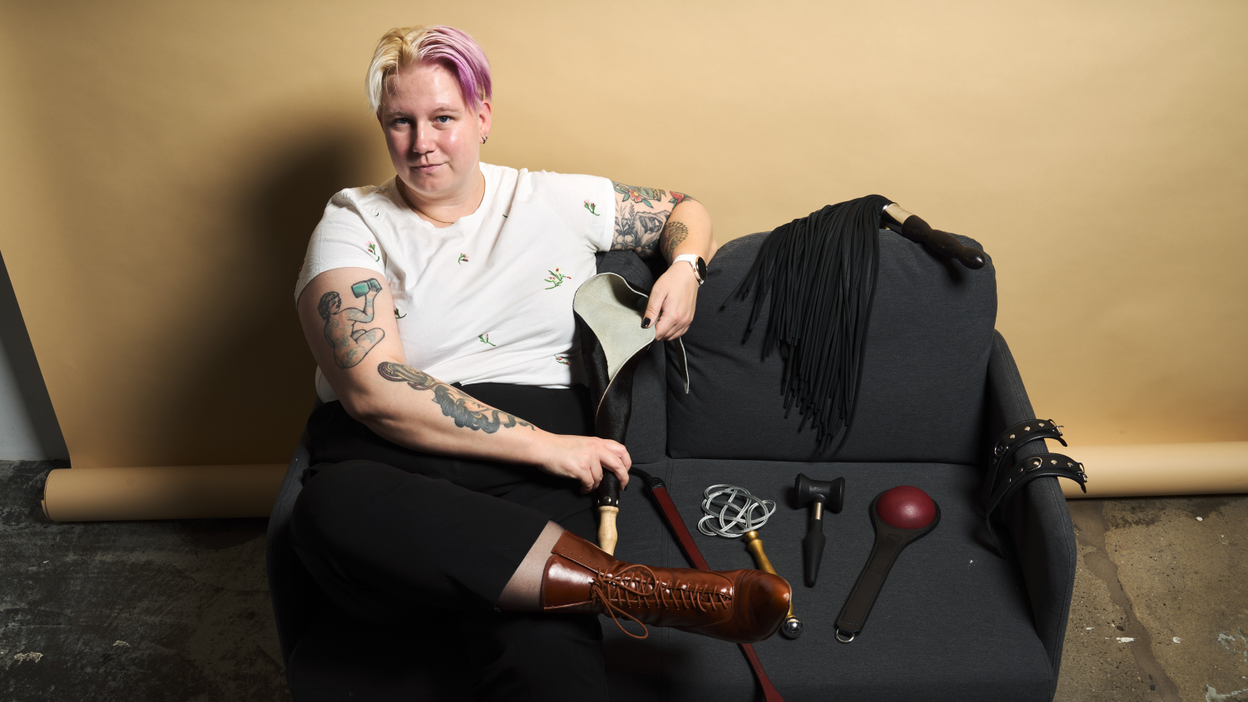 A person is sitting on a couch with a large selection of BDSM sex toys