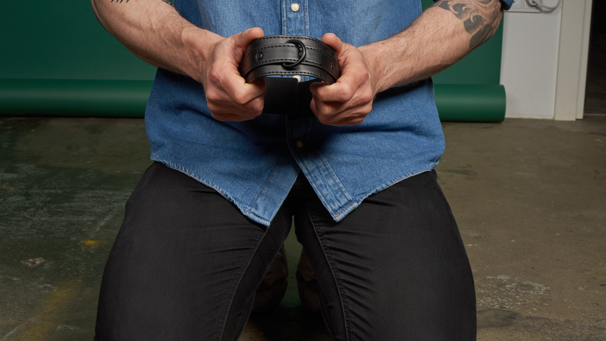 A person on their knees with a BDSM collar in their hands