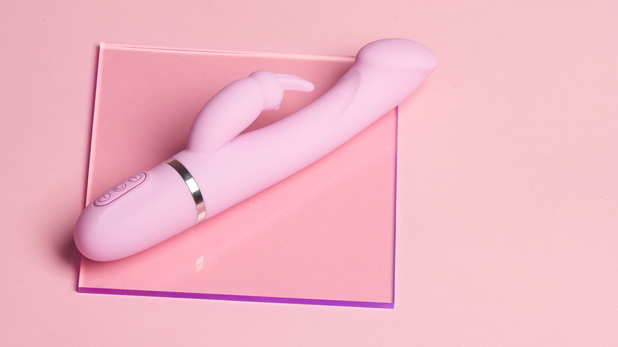Rosa rabbitvibrator som ligger på en glassplate på en rosa bakgrunn
