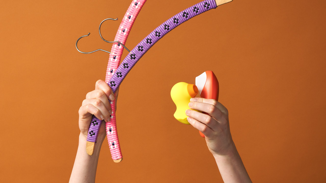 Hands holding two clitoral stimulators and two coat hangers