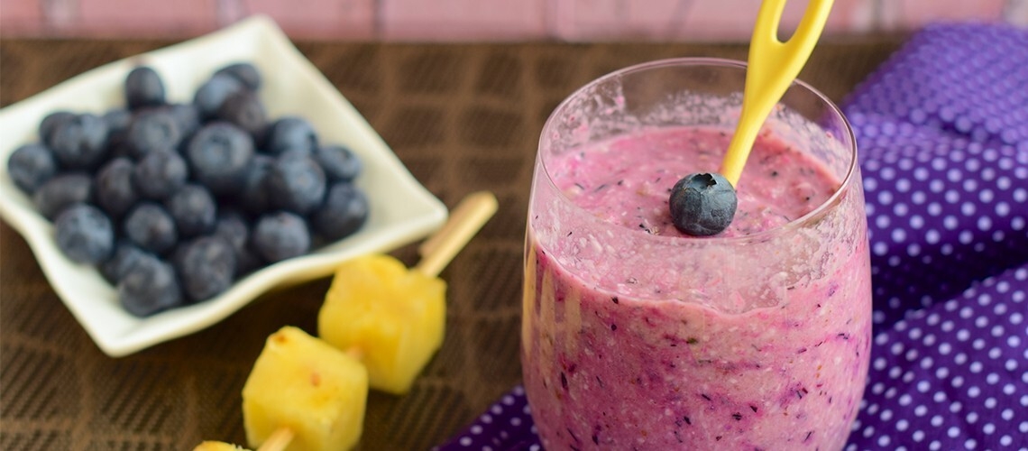 Blueberry pineapple smoothie in a glass, garnished with pineapple slices