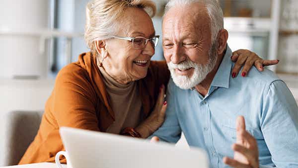 Μια γυναίκα αγκαλιάζει έναν άνδρα ενώ κοιτάζει τον υπολογιστή. Χαμογελάνε
