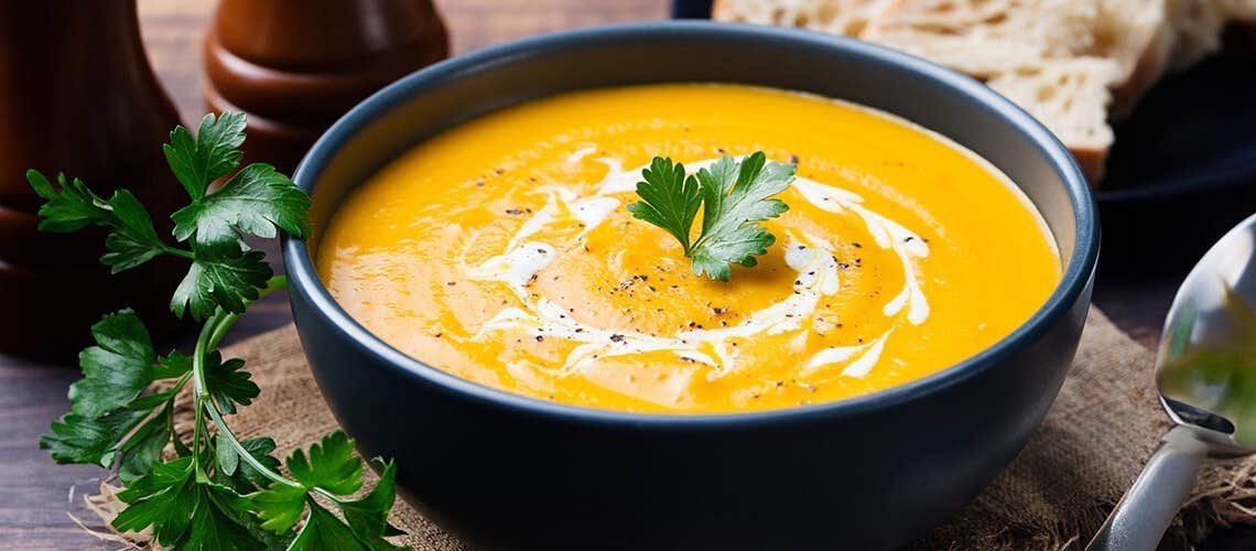 Bowl of creamy pumpkin soup garnished with fresh herbs Κολοκυθόσουπα με Κάρυ & Γάλα Καρύδας