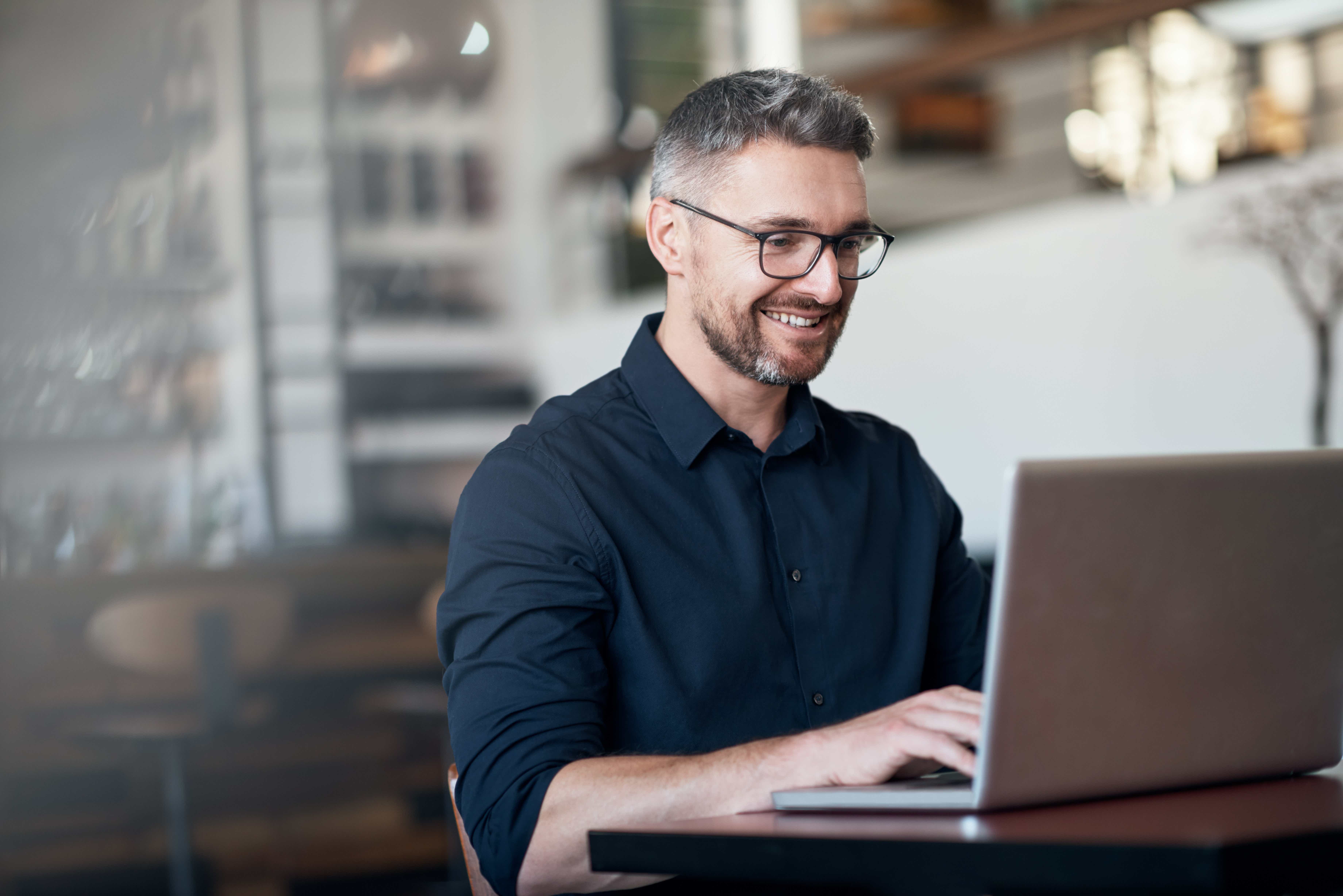 Ένας άντρας με γυαλιά που εργάζεται σε ένα φορητό υπολογιστή και χαμογελά