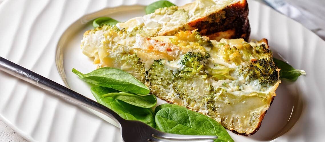 A slice of broccoli quiche in a plate, decorated with spinach leaves Κις Λορέν με Μπρόκολο & Τσένταρ