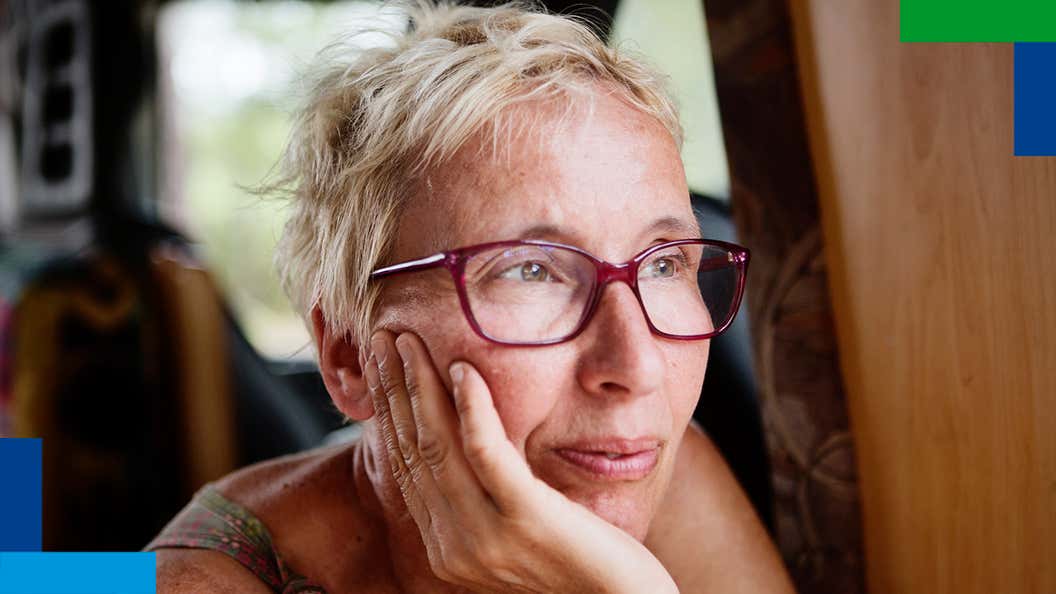 Μια γυναίκα με κοντά μαλλιά και γυαλιά κοιτάζει έξω από το παράθυρο