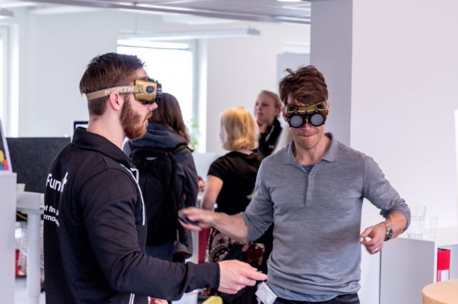 two men playing nintendo switch while wearing vision impairment goggles