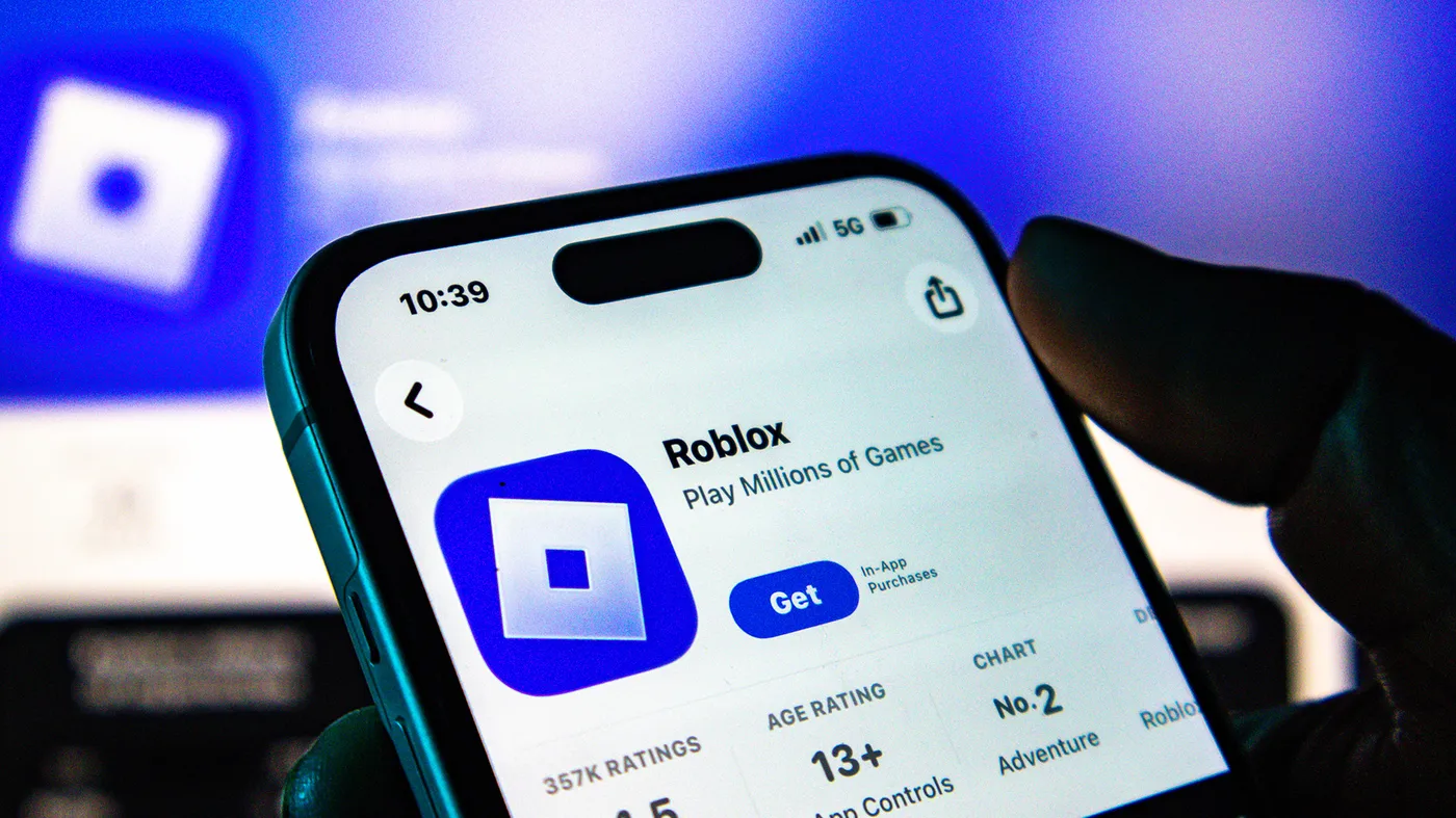 A photo of a phone displaying the Roblox page on the iOS App Store. A photo of a phone displaying the Roblox page on the iOS App Store.