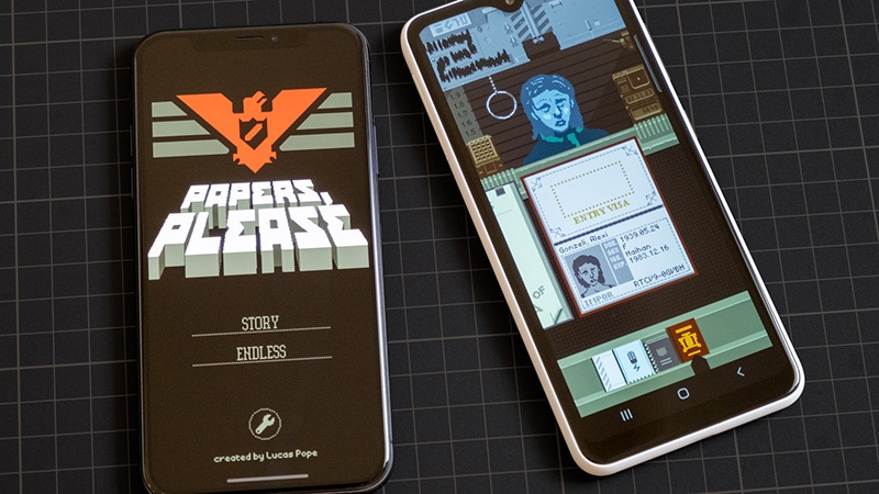 A photograph of Papers, Please playing on an iPhone and Android mobile phone. A photograph of Papers, Please playing on an iPhone and Android mobile phone.