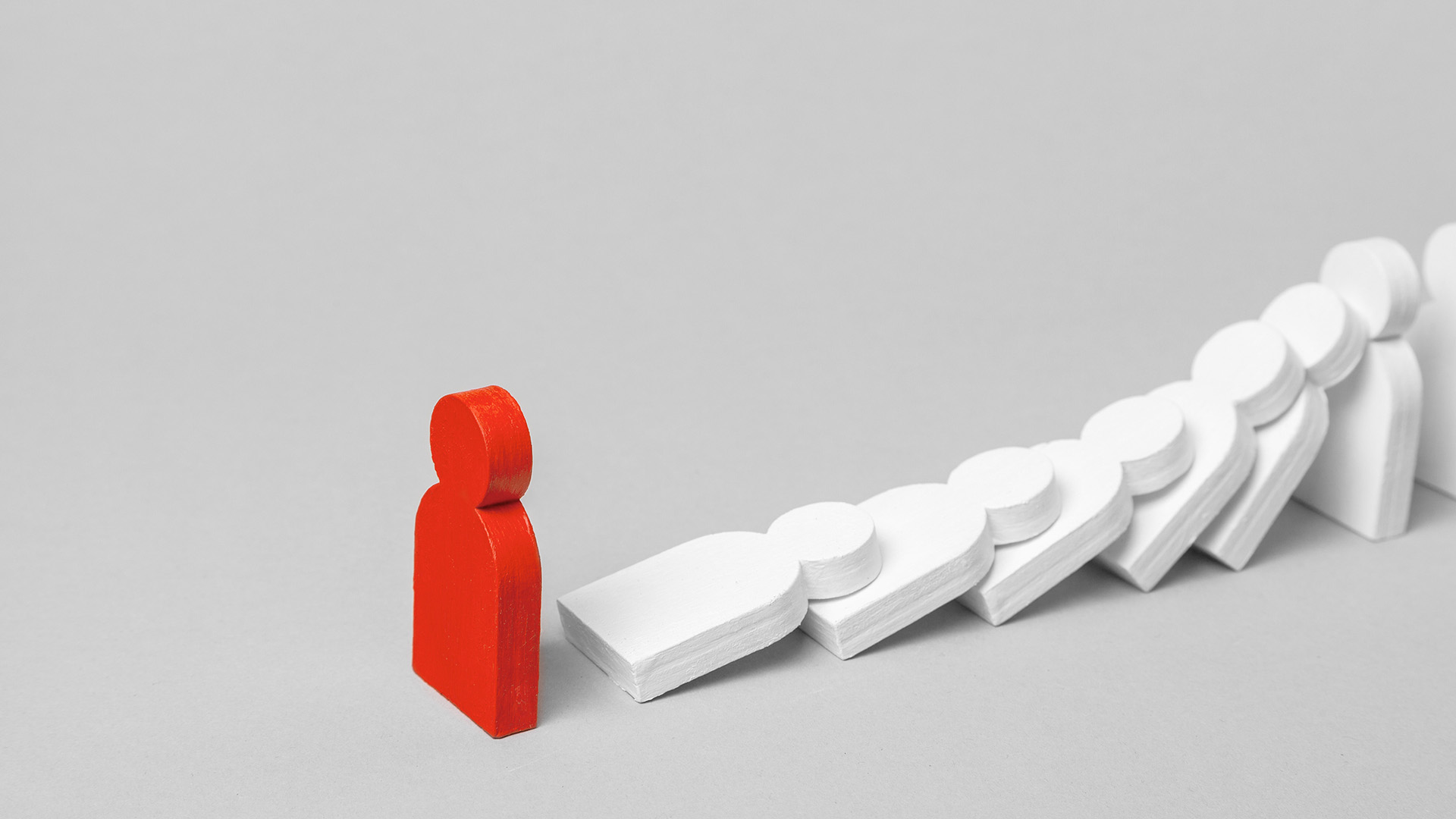 A red person-shaped domino stands tall while other white dominoes are knocked over.