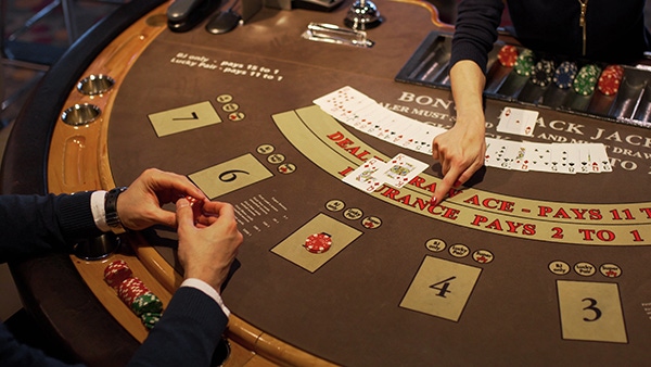 A top-down photo of a Blackjack table. A man holds cards in the foreground while a woman deals the next hand.