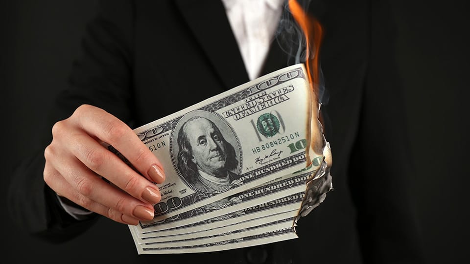 A woman holds hundred-dollar bills that are on fire. A woman holds hundred-dollar bills that are on fire.