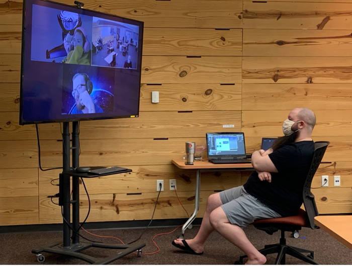 Members of a game development team meet both on campus and virtually over Zoom.