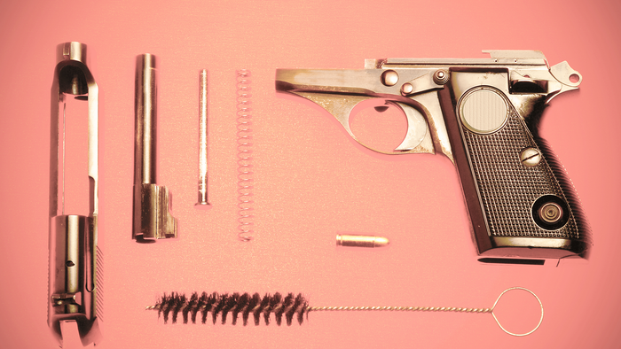 A disassembled handgun, with the components laid out on a pink background. A disassembled handgun, with the components laid out on a pink background.