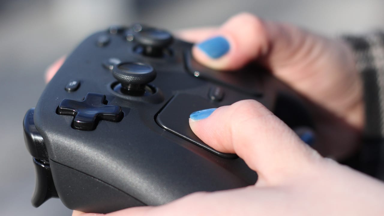 A person with blue fingernails holds a Steam Controller. The D-Pad is in focus. A person with blue fingernails holds a Steam Controller. The D-Pad is in focus.