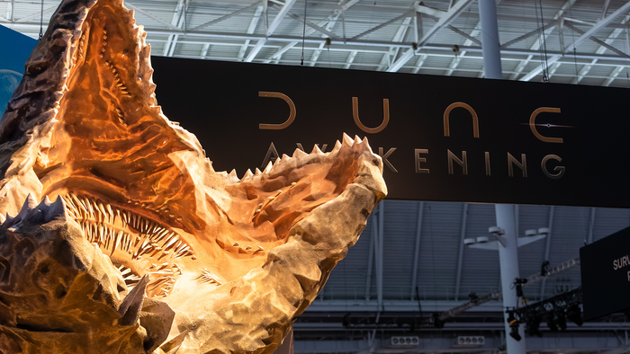 A Sandworm from Dune Awakening, in front of a sign for the game. A Sandworm from Dune Awakening, in front of a sign for the game.