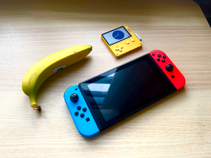 Playdate nestled next to a Nintendo Switch and banana