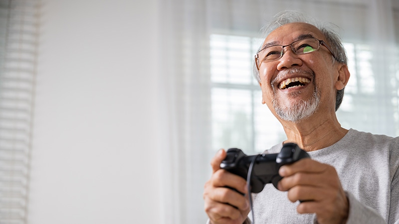 An older man holds a PlayStation controller.