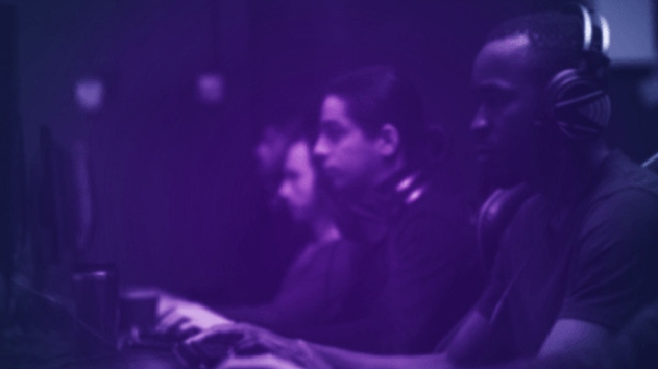 A group of people play video games on a computer. A purple filter obscures their features.