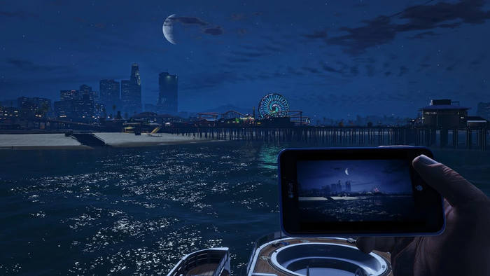 A screenshot from Grand Theft Auto 5, including the player on a yacht taking a photo of Del Perro Beach with their iFruit phone at night, with another boat and the Los Santos skyline in the distance. A screenshot from Grand Theft Auto 5, including the player on a yacht taking a photo of Del Perro Beach with their iFruit phone at night, with another boat and the Los Santos skyline in the distance.