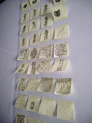 A wall with a grid laid out of yellow Post-It notes, each bearing a sketch in black ink.