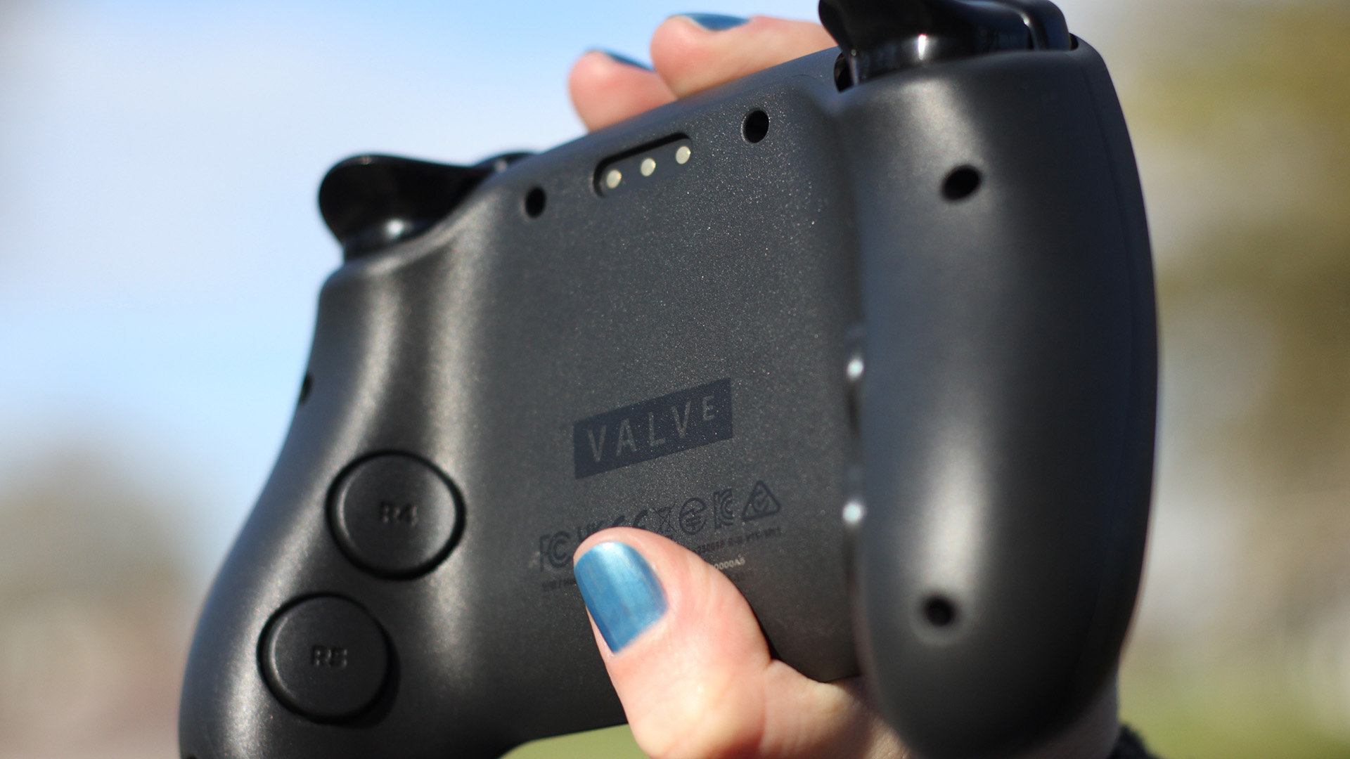 A person with blue fingernails holds up a Steam Controller. The rear is visible.