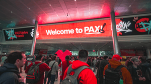 A digital banner welcoming attendees to PAX East, with several con-goers in the foreground. A digital banner welcoming attendees to PAX East, with several con-goers in the foreground.