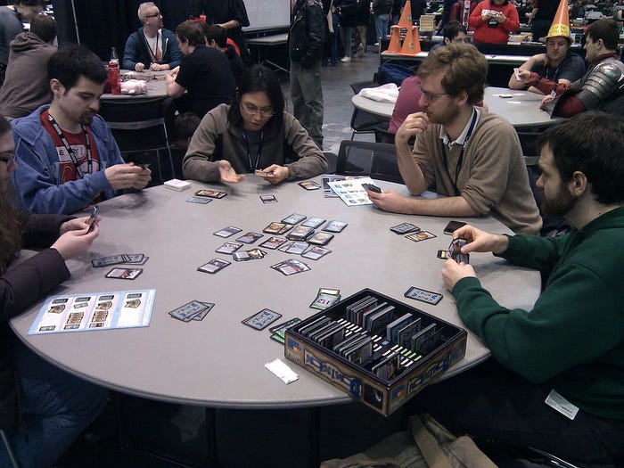 Four players gather around a table to play the card game Dominion.