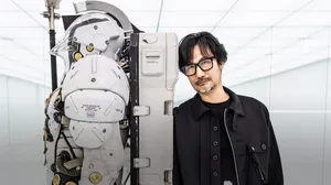 A photograph of Hideo Kojima standing next to studio mascot Ludens. A photograph of Hideo Kojima standing next to studio mascot Ludens.