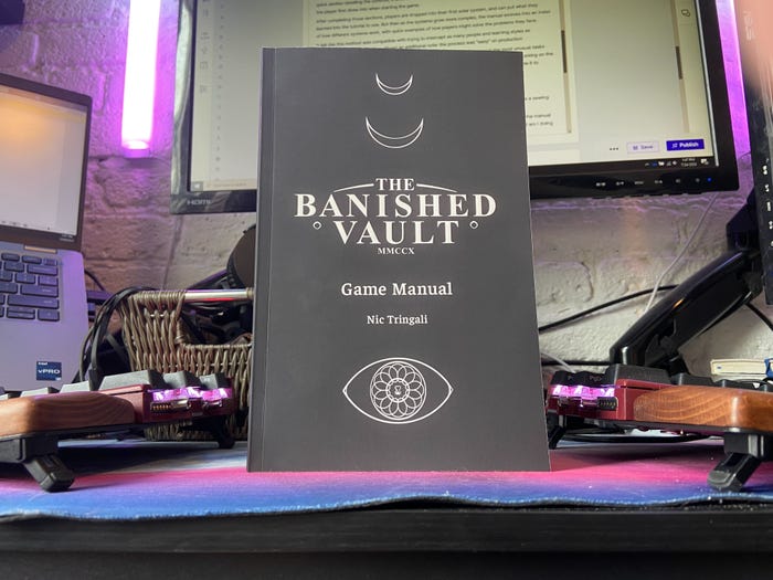 A photograph of The Banished Vault's manual. It sits on a desk, backlit by purple and blue lights.