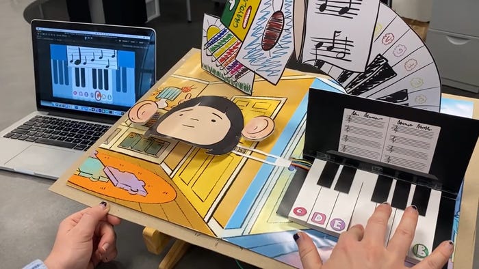 hand on a paper piano controller and piano keys on screen