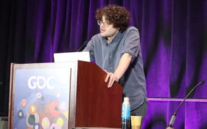curly-haired man with glasses stands at podium and places both of his hands on its sides