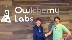 Andrew Eiche and Devin Reimer shake hands in front of the Owlchemy Labs sign.