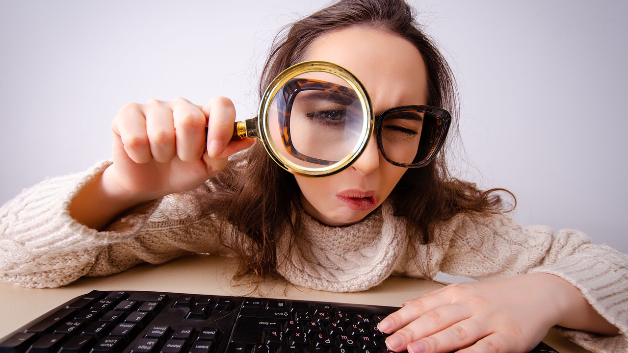 A woman looks at a computer through a magnifying glass. A woman looks at a computer through a magnifying glass.