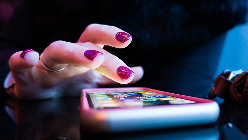A hand with fingernail polish on it taps on an iPhone. A hand with fingernail polish on it taps on an iPhone.
