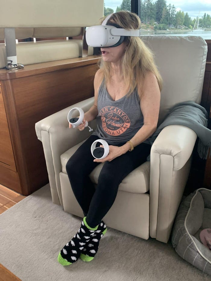 A picture of game designer Roberta Williams, wearing a VR headset as she sits in a white leather chair.