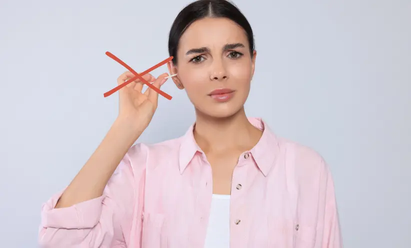 So sollte man seine Ohren nicht reinigen. Frau reinigt am Bild ihr rechtes Ohr mit einem Wattestäbchen.webp