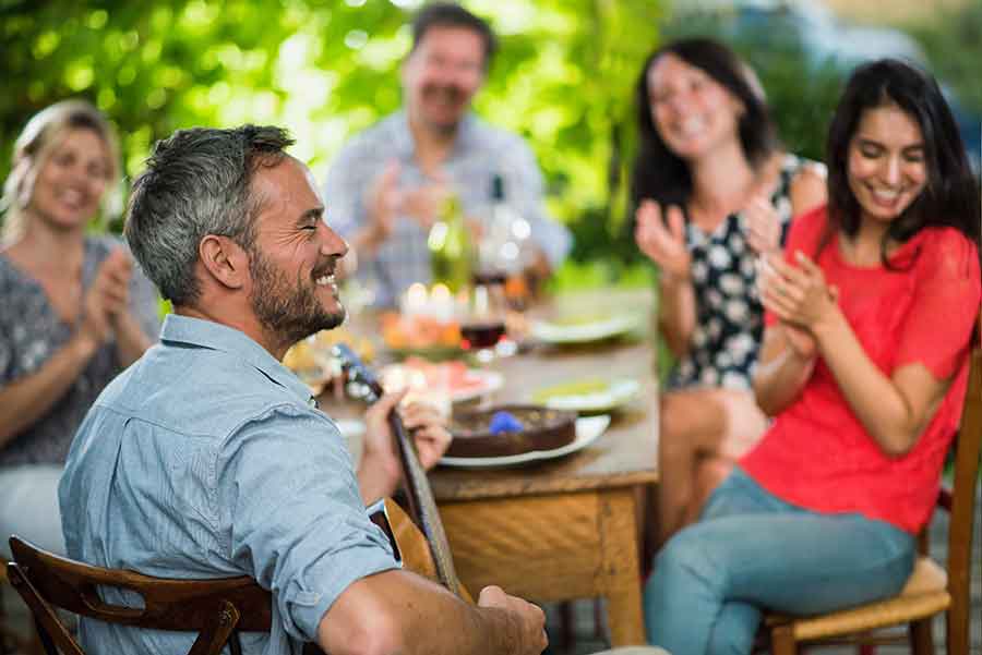 man-speelt-gitar-aan-een-tafel-mensen-om-zich-heen.jpg