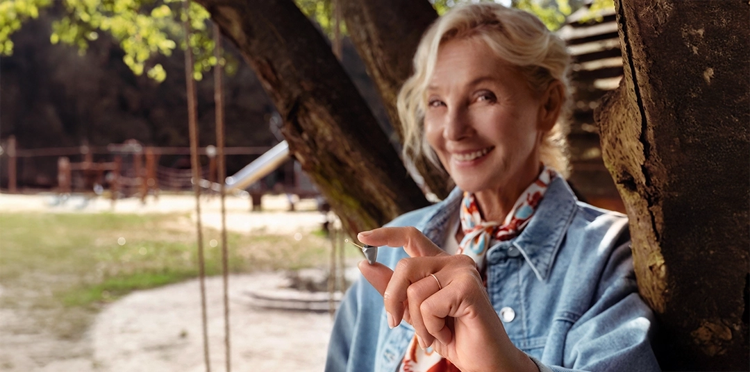 Frau auf Spielplatz hält Mini Hörgerät in der Hand