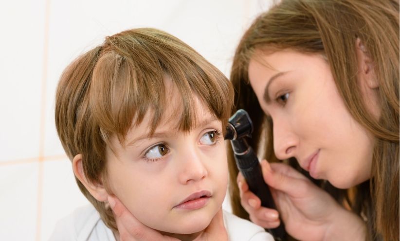 Ärztin untersucht das Ohr eines Kindes mit einem Otoskop – typische Untersuchung zur Diagnose einer Mittelohrentzündung (Otitis media)
