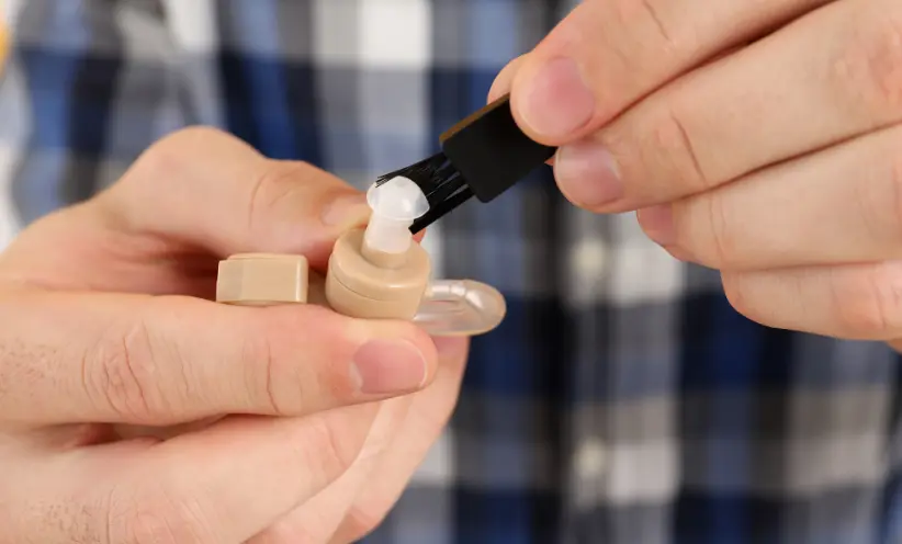 Mann reinigt das Hörgerät mit einem Bürstchen.webp