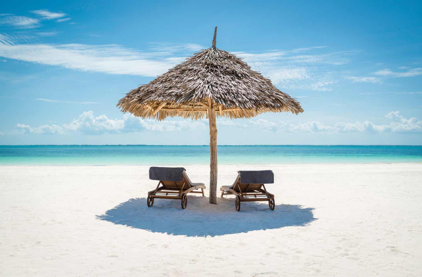 Tansania beste Reisezeit: zwei hölzerne Sonnenliegen am weißen Sandstrand