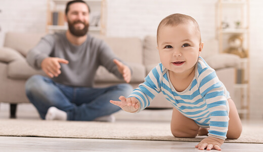 Cierra a una madre asiática sosteniendo a su pequeño bebé aprendiendo a caminar en el suelo de madera en casa. Un niño lindo disfrutando de los primeros pasos con mamá.
