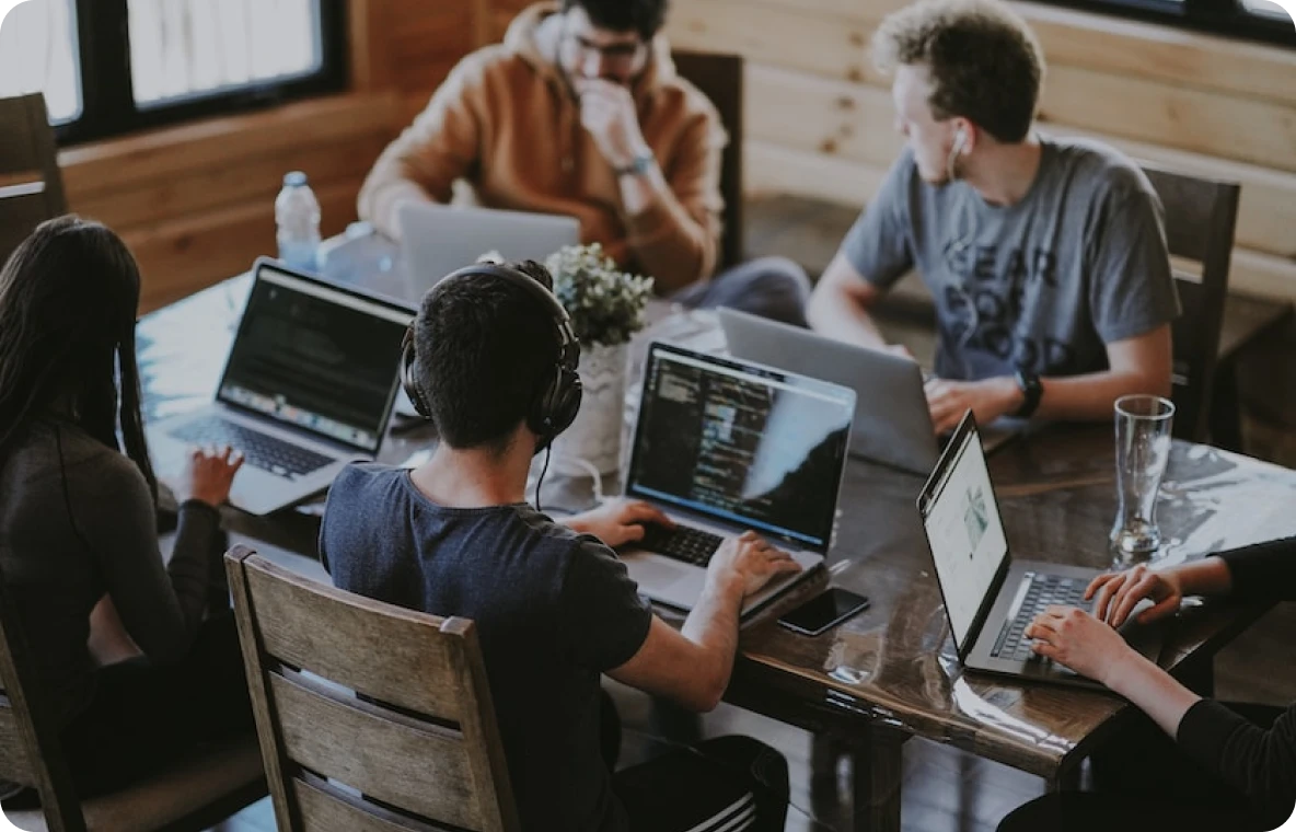 A diverse group of individuals sitting around a table, engrossed in their work on laptops.