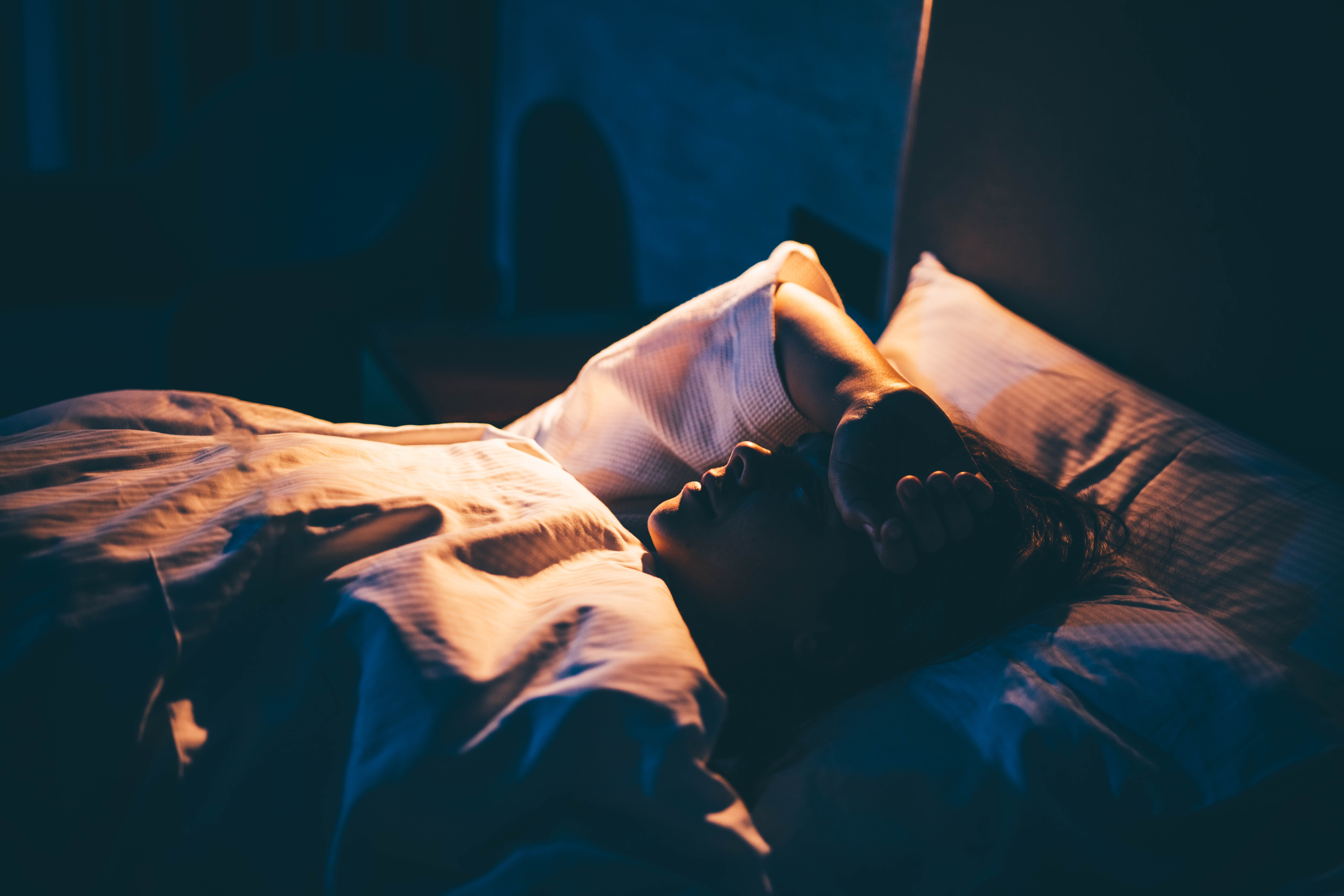 The image depicts a person lying in bed, seemingly asleep or deeply relaxed, bathed in a cool, predominantly blue and white light.