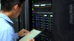 An IT technician inspects and manages a server rack in a data center using a tablet An IT technician inspects and manages a server rack in a data center using a tablet