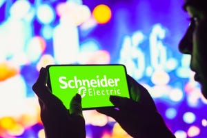 In this photo illustration, a silhouetted woman holds a smartphone with the Schneider Electric logo displayed on the screen.
