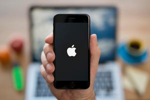 A hand holds an iPhone which displays the Apple logo.