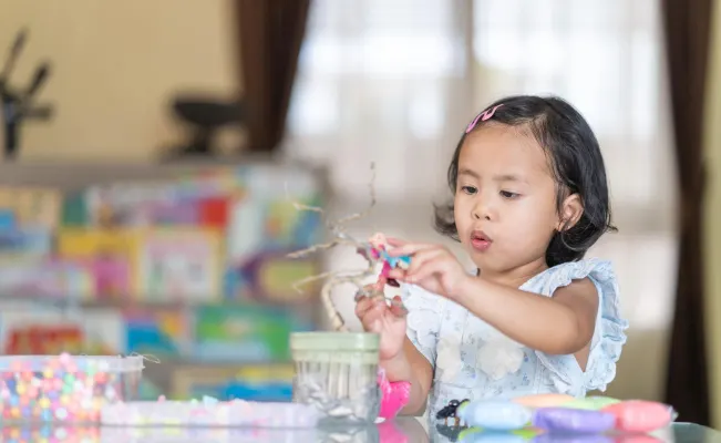 Little girl focused on a craft project with colorful materials on the table