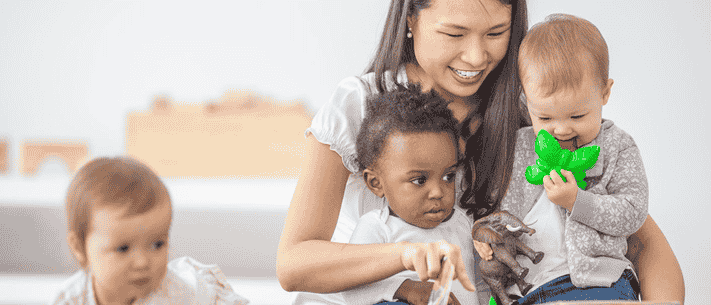Caregiver Holding Two Infants with Toys in a Daycare Setting, Creating a Warm and Nurturing Environment